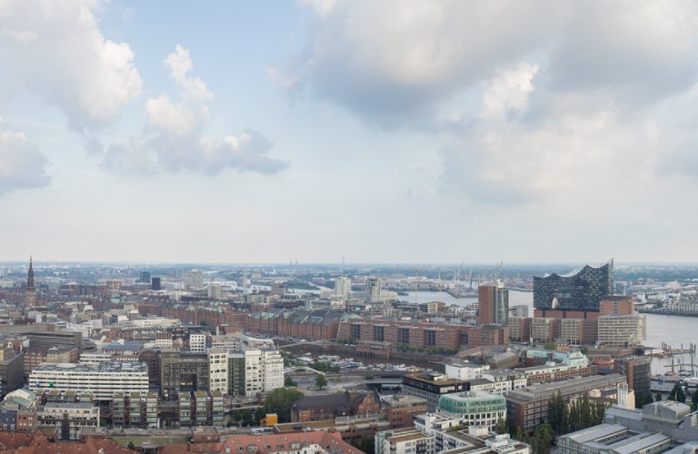 Blick über die Skyline von Hamburg mit der Elbphilharmonie und dem Hafen im Vordergrund.