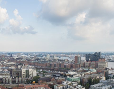Blick über die Skyline von Hamburg mit der Elbphilharmonie und dem Hafen im Vordergrund.
