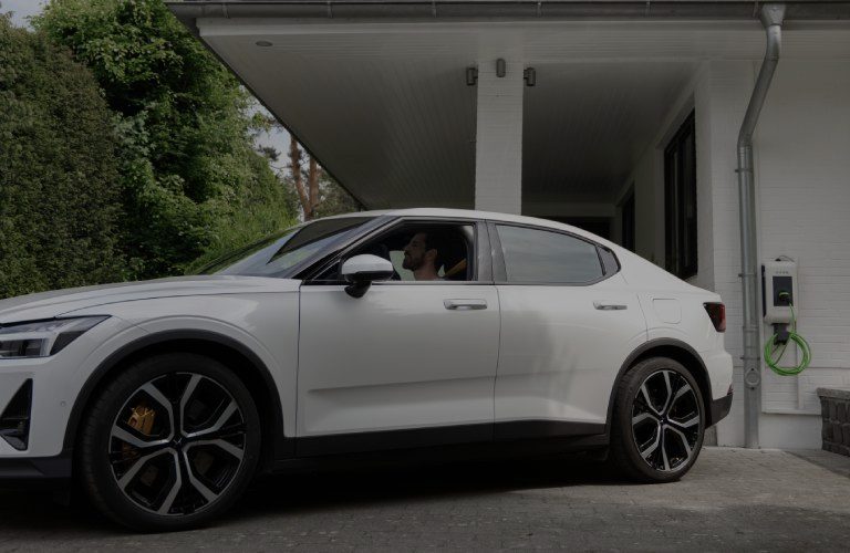 Hinweis: 85 € THG-Prämie für 2025 sichern! Ein Mann sitzt in einem Elektroauto vor einem Einfamilienhaus.