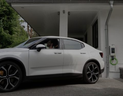 Hinweis: 85 € THG-Prämie für 2025 sichern! Ein Mann sitzt in einem Elektroauto vor einem Einfamilienhaus.