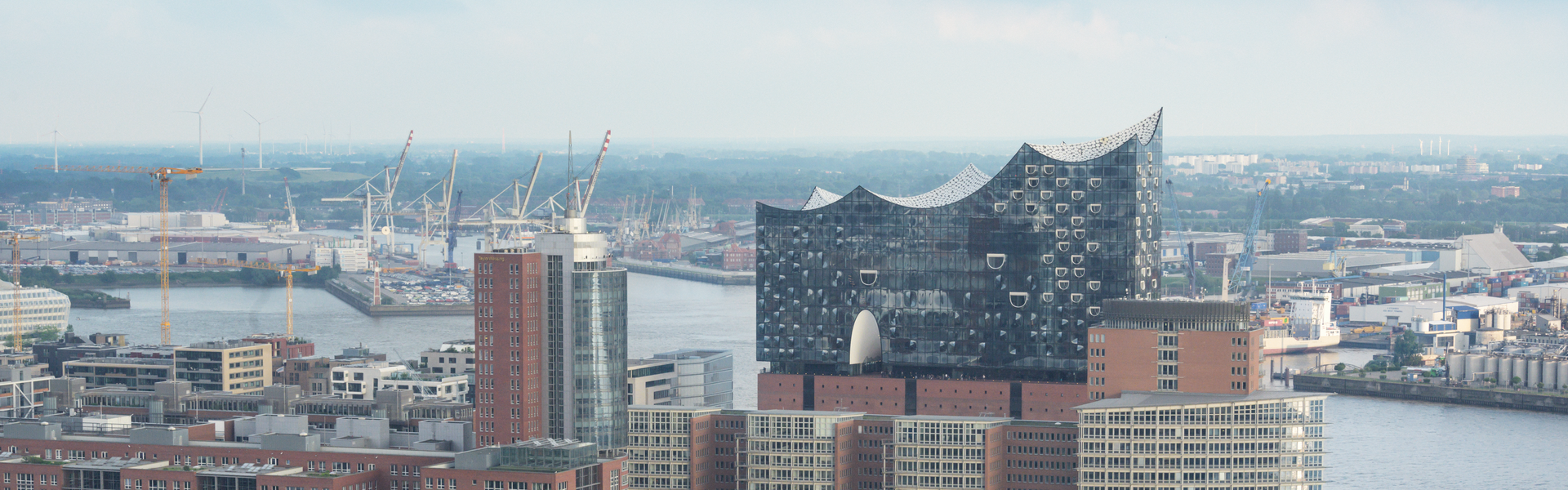 Blick über die Skyline von Hamburg mit der Elbphilharmonie im Vordergrund und dem Hafen dahinter.
