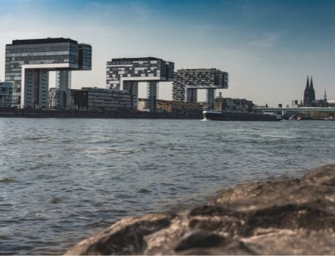 Blick auf die Stadt Köln mit dem Rhein und den Kranhäusern im Vordergrund und dem Kölner Dom im Hintergrund.