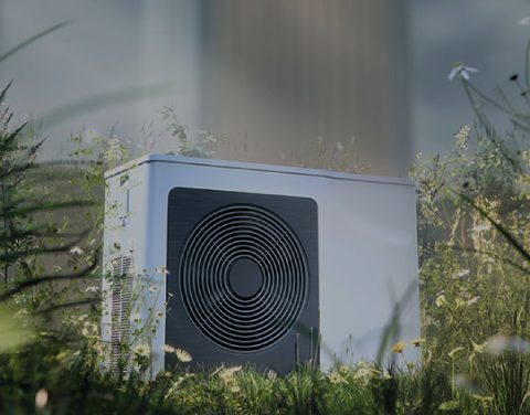 Moderne Wärmepumpe steht auf einer Wiese umringt von vielen verschiedenen Blumen und Gräsern.