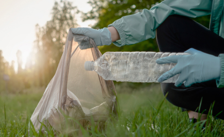 Hand legt Plastikflasche in Mülltüte