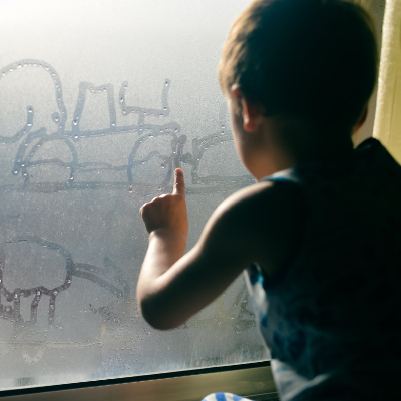 Ein kleiner Junge schreibt an einer beschlagenen Fensterscheibe