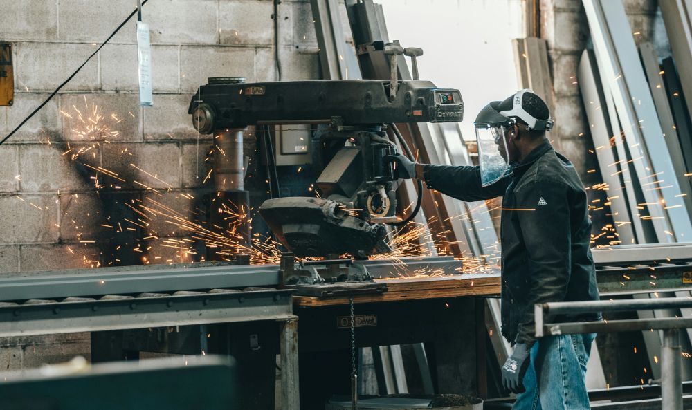 Arbeiter mit Schutzvisier bearbeitet Metall an einer Industriemaschine, Funken sprühen.
