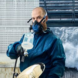 Dieses Bild zeit einen Mann in Arbeitskleidung mit einer Atemschutzmaske und einem Blechblasinstrument und verdeutlicht das Thema CO2 Management