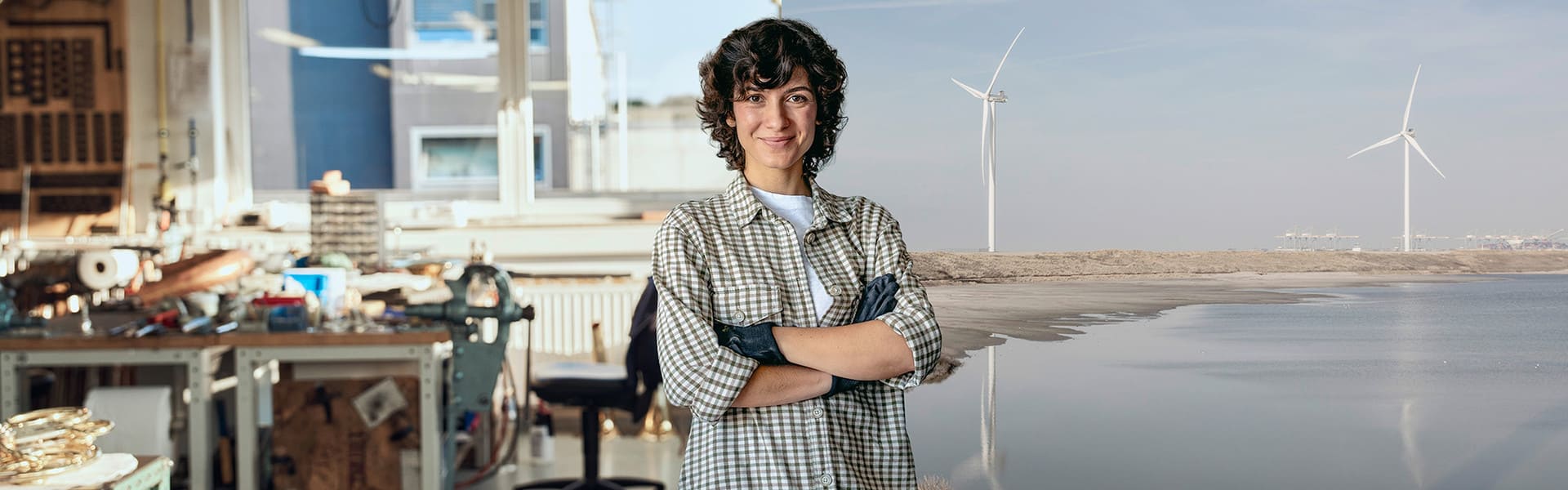 Handwerkerin steht im Vordergrund. Eine Werkstatt und eine Onshore Windkraftanlage sind im Hintergrund.