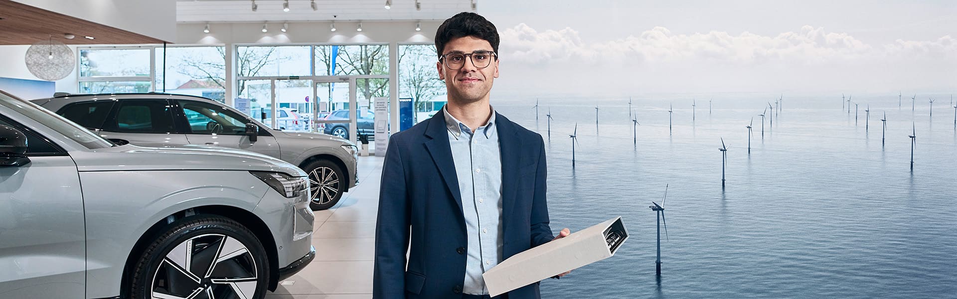 Mann hält Aktenordner. Im Hintergrund ist ein Autohaus und ein Offshore Windpark zu sehen.