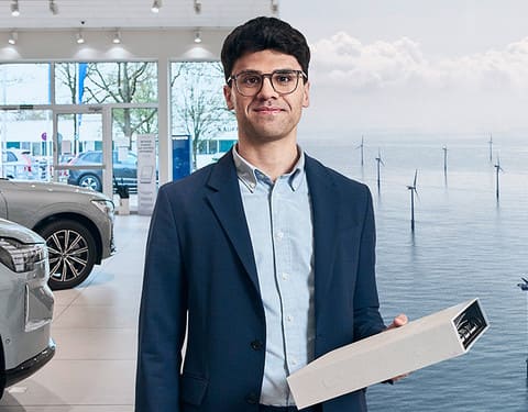 Mann hält Aktenordner. Im Hintergrund ist ein Autohaus und ein Offshore Windpark zu sehen.