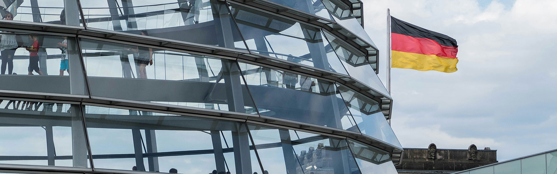 Ein Ausschnitt der Reichstagskuppel ist sichtbar. Dahinter weht eine Deutschlandfahne.