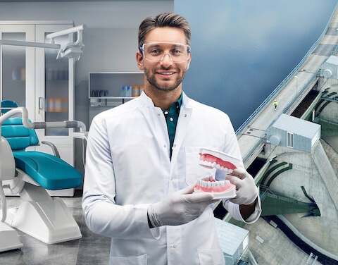 Ein Zahnarzt steht mit einem Gebiss in der Hand in der Praxis.