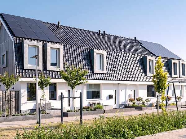 Reihenhäuser mit dunklen Dächern, auf denen Solarpanels installiert sind, davor eine gepflegte Straße mit jungen Bäumen und Grünstreifen – modernes Wohngebiet mit Fokus auf Nachhaltigkeit.