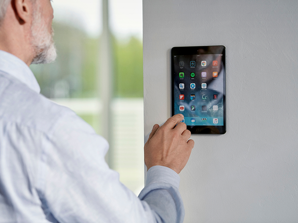 Älterer Mann bedient ein an der Wand montiertes Smart-Home-Panel mit verschiedenen Steuerungsfunktionen – modernes Zuhause mit digitaler Haustechnik.