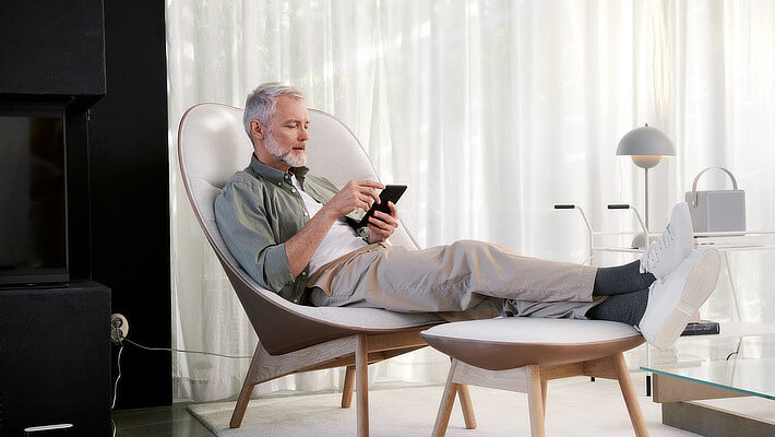 Mann im Wohnzimmer auf Stuhl mit Smartphone in der Hand
