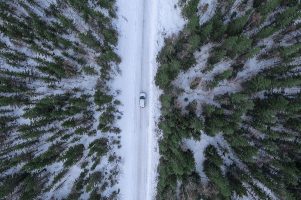 Auto fährt im Schnee durch Wald Vogelpespektive