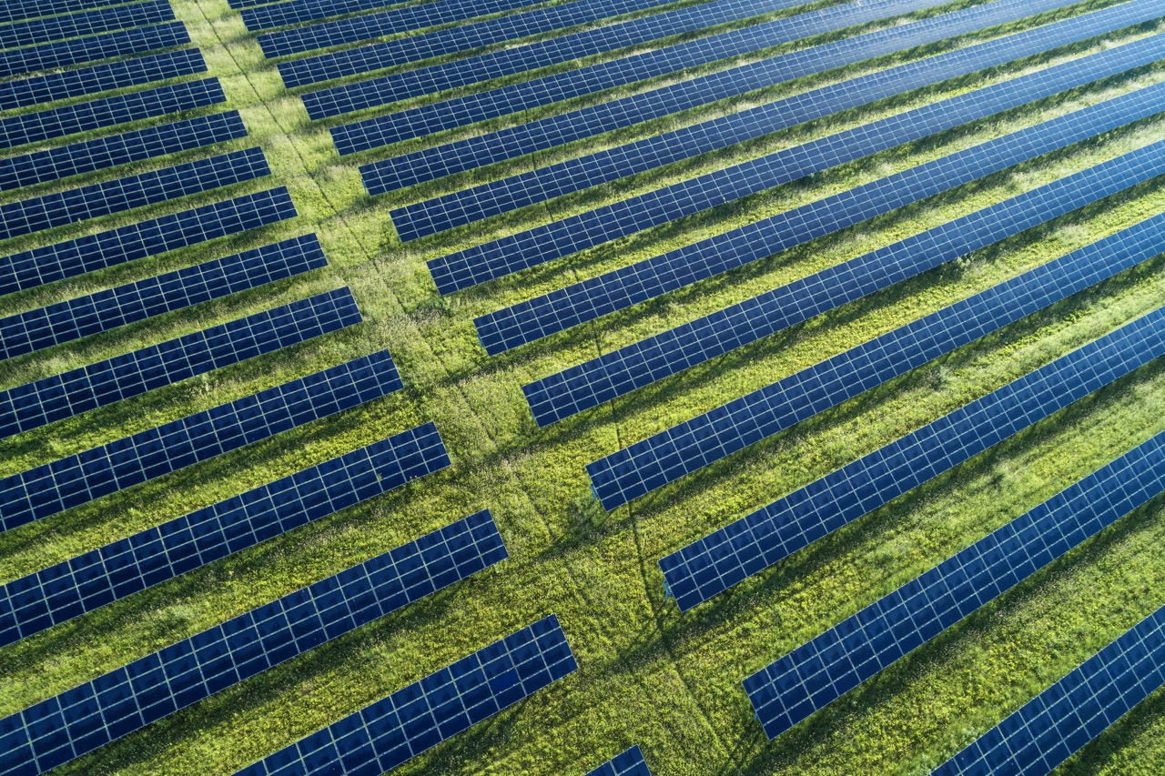 Luftaufnahme eines Solarparks mit vielen Reihen von blauen Solarpaneelen, die auf einer grünen Wiese installiert sind.