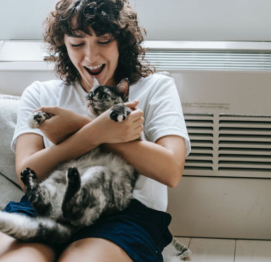 Junge Frau mit einer Katze an der Elektrospeicherheizung angelehnt