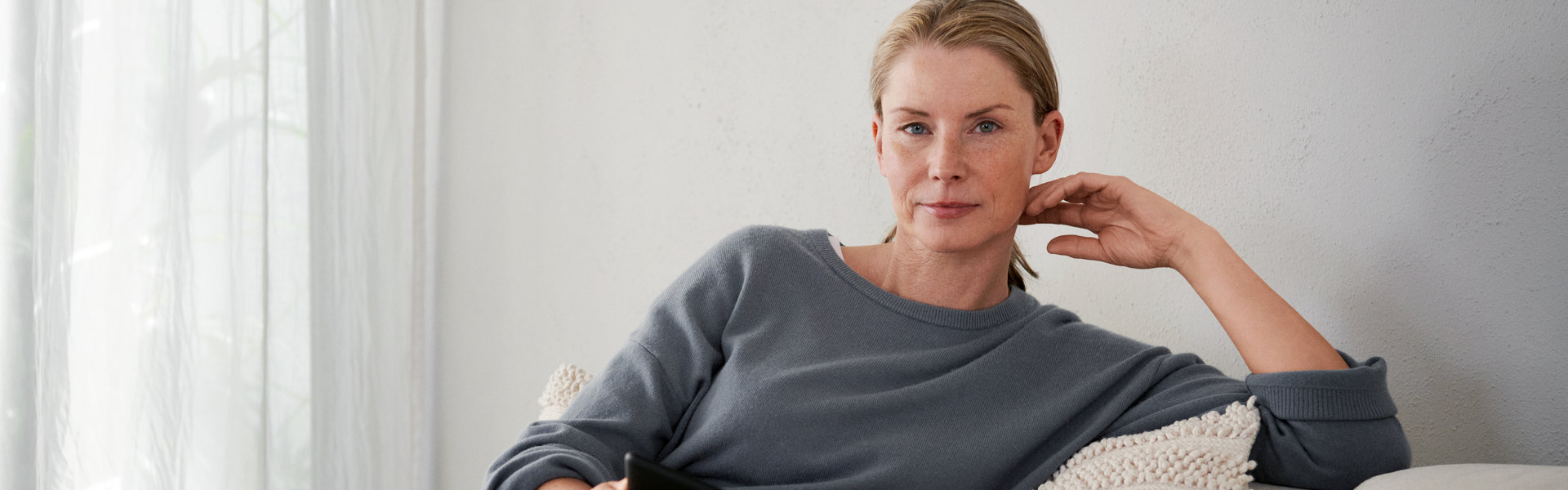 Eine Frau sitzt entspannt auf einem Sofa und schaut in die Kamera.