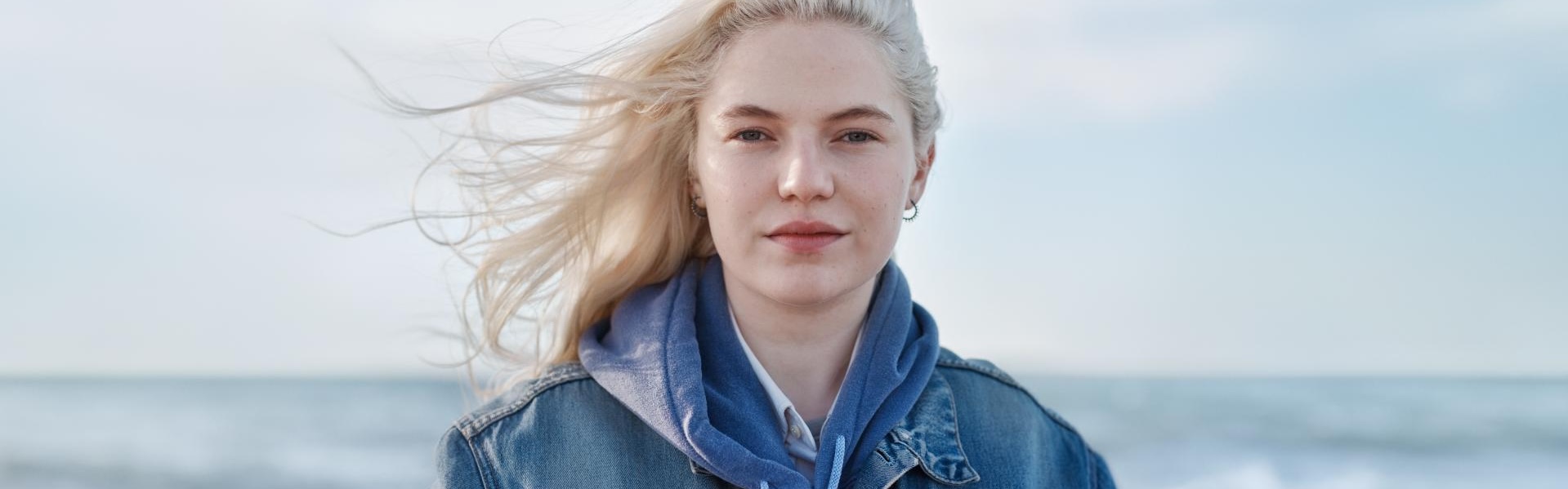 Frau steht vor einem Meer und die Haare wehen im Wind.
