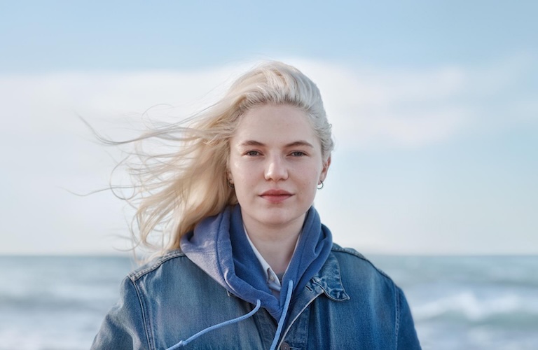 Frau steht vor einem Meer und die Haare wehen im Wind.