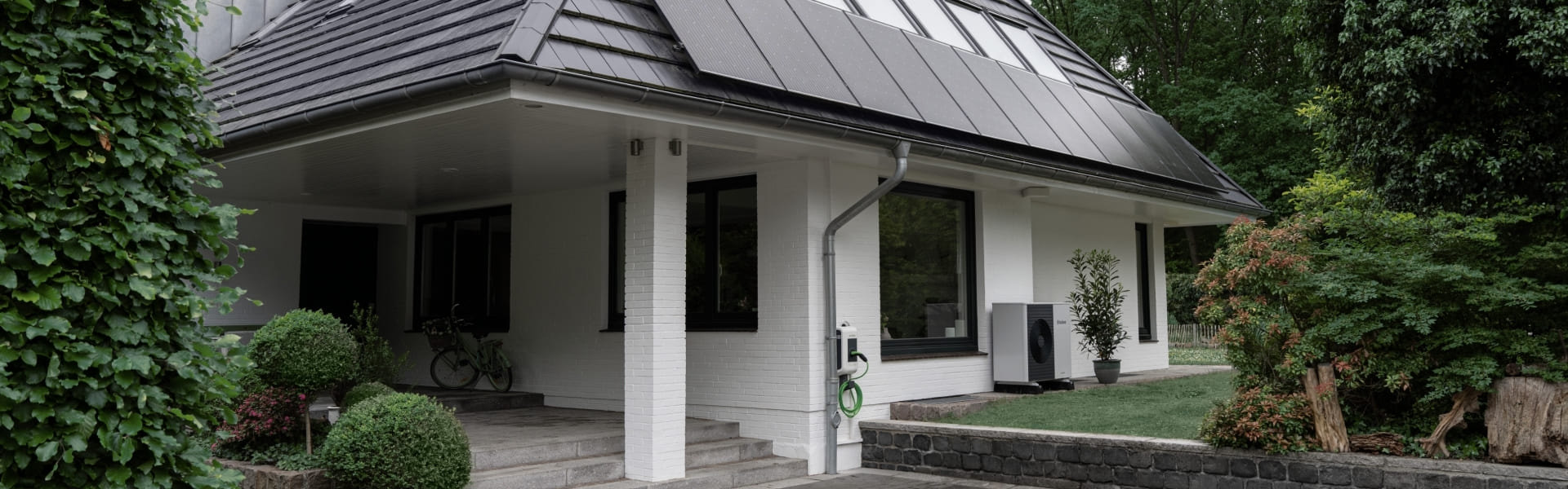 Aussenansicht eines Einfamilienhauses mit Solarmodulen auf dem Dach und einer Wärmepumpe im an der Hausfassade.
