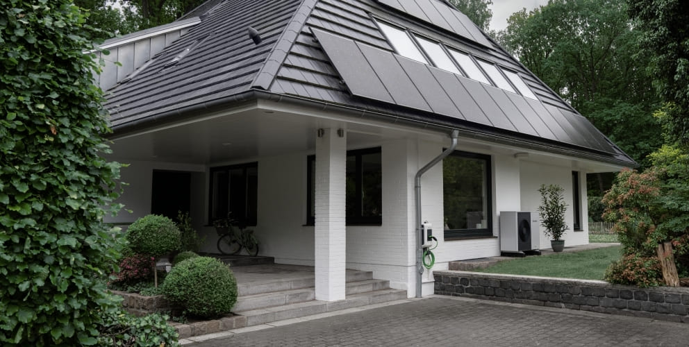 Aussenansicht eines Einfamilienhauses mit Solarmodulen auf dem Dach und einer Wärmepumpe im an der Hausfassade.