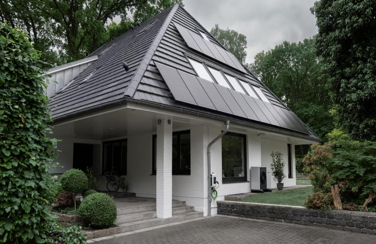 Aussenansicht eines Einfamilienhauses mit Solarmodulen auf dem Dach und einer Wärmepumpe im an der Hausfassade.