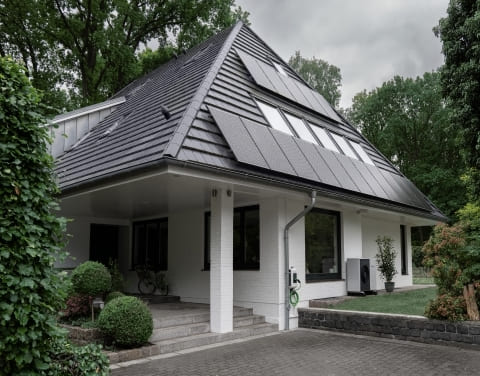Aussenansicht eines Einfamilienhauses mit Solarmodulen auf dem Dach und einer Wärmepumpe im an der Hausfassade.