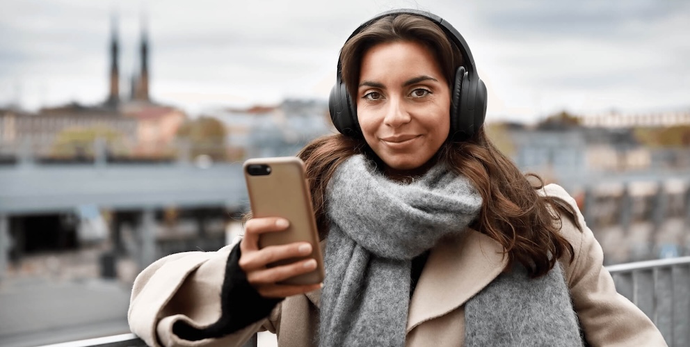 Frau steht draußen auf einer Brücke und schaut aufs Handy.