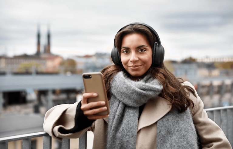 Frau steht draußen auf einer Brücke und schaut aufs Handy.