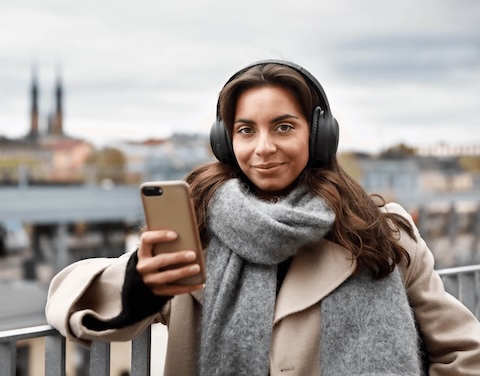 Frau steht draußen auf einer Brücke und schaut aufs Handy.