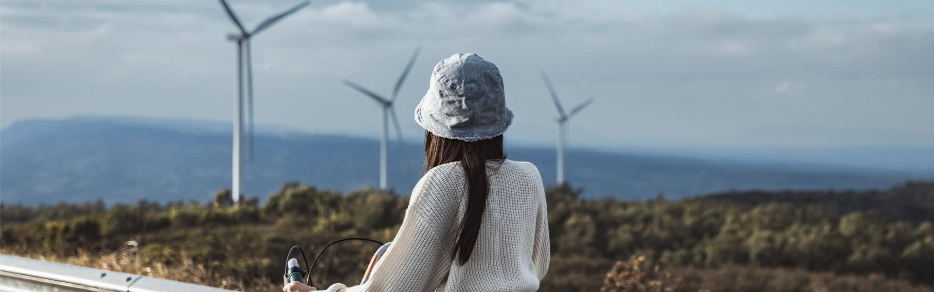 Eine Person von hinten auf dem Fahrrad. Sie schaut richtung Meer auf einen Onshore-Windpark.