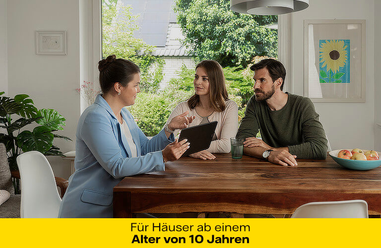 Eine Frau mit einem hellblauen Blazer sitzt gemeinsam mit einem Mann und einer Frau an einem Esstisch. Sie hält ein Tablet in der Hand und erklärt den beiden etwas. Sie befinden sich in einem modernen und hellen Esszimmer.