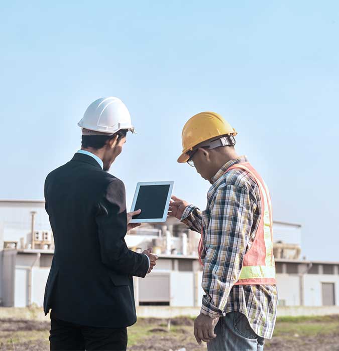 zwei Männer stehen vor einem Bau und schauen auf Tablet
