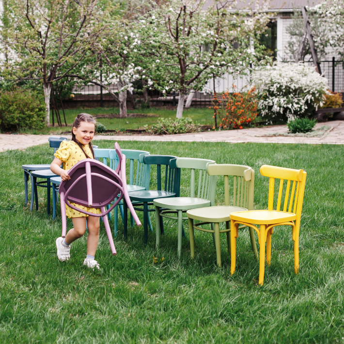 Kind baut bunte Stuhlreihe im Garten auf